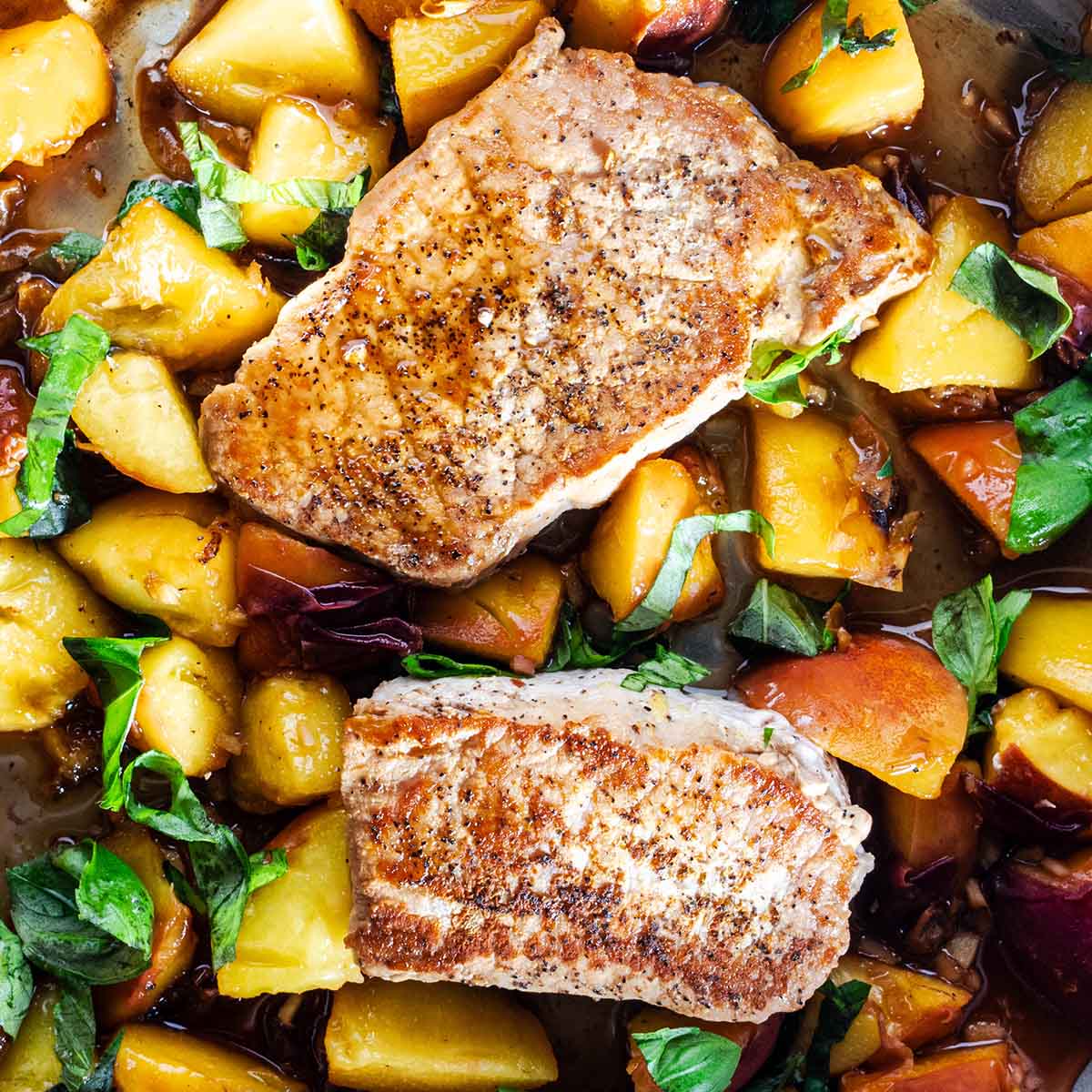 2 boneless pork chops in a skillet with a sauce of peaches, ginger, brown sugar, and basil