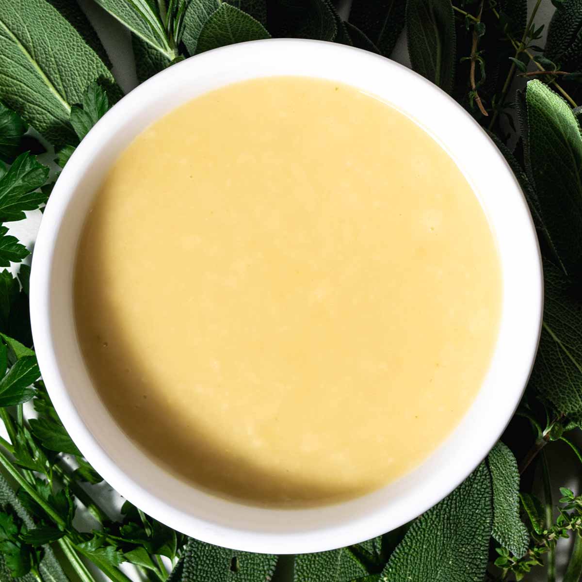 A container of Thanksgiving gravy on a bed of herbs