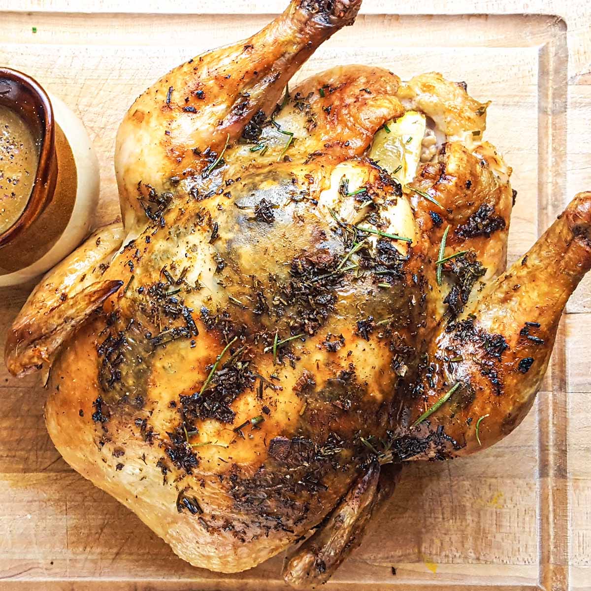 An herb roasted chicken ready to carve for Thanksgiving, on a wood cutting board