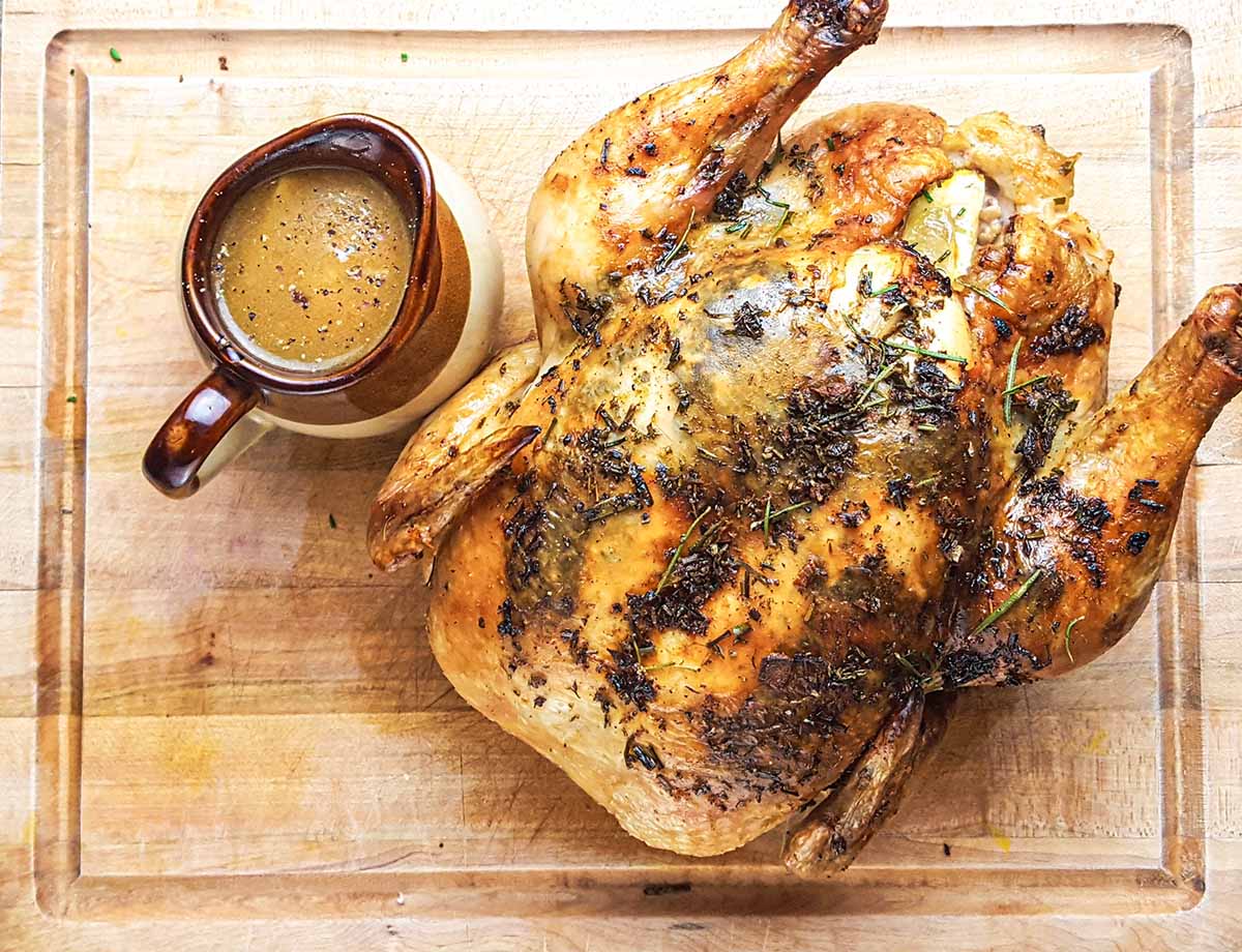 A Thanksgiving roasted chicken with a side of gravy, on a light wood cutting board