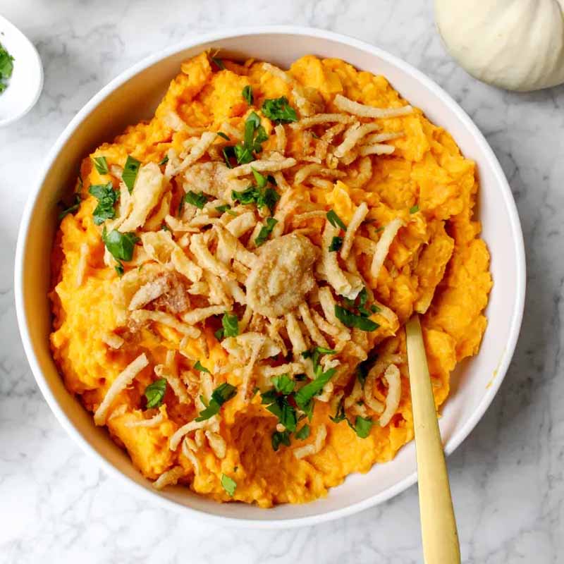 A bowl of apple cider sweet potatoes topped with crispy onions. A friendsgiving recipe by Yes to Yolks.
