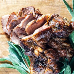 Apple cider braised pork shoulder on a serving board surrounded by fresh sage leaves