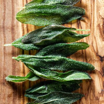Fried sage leaves on an olive wood board, topped with salt.