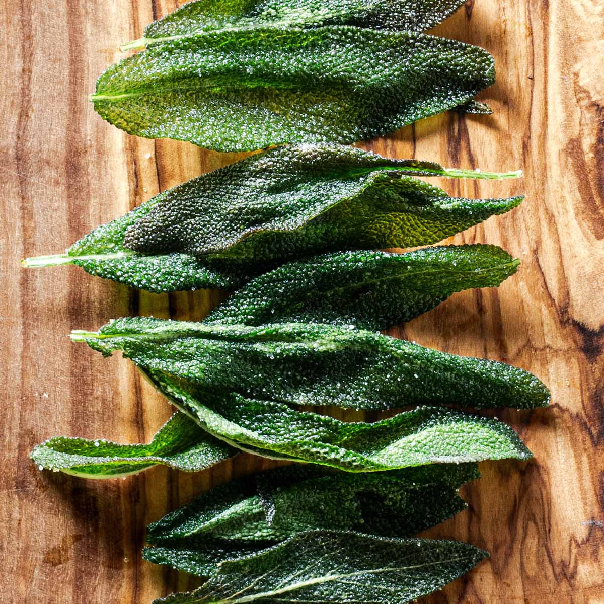 Fried sage leaves on an olive wood board, topped with salt.