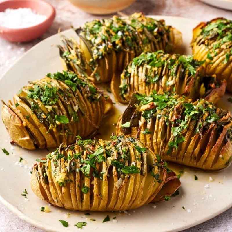 A plate of hasselback potatoes topped with fresh herbs. Recipe from Love and Lemons.