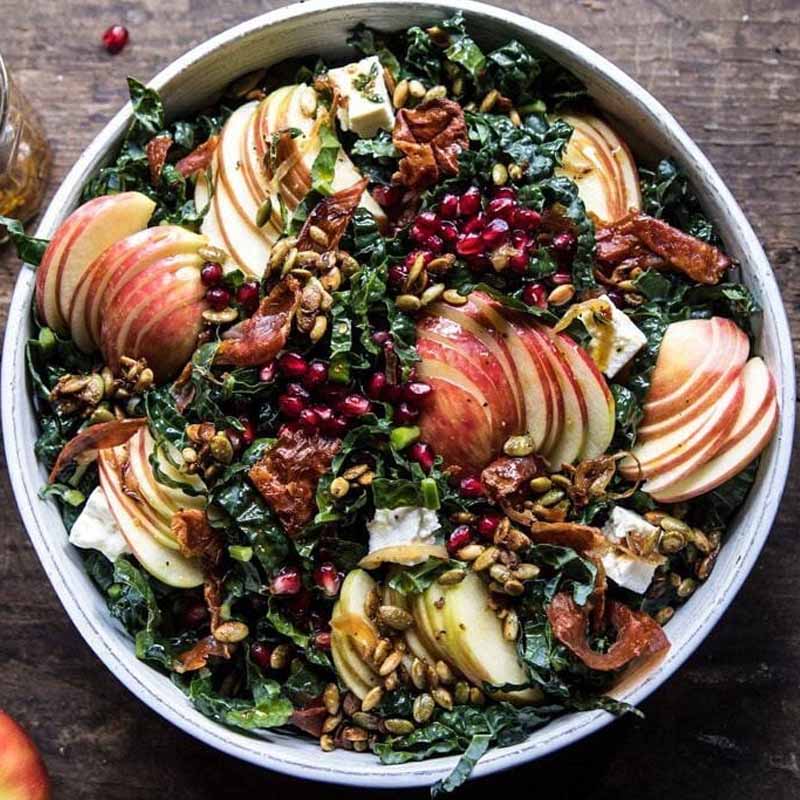 A fall salad on a plate with kale, apples, and pomegranate seeds. Use Pink Lady apples if you're bringing this to Friendsgiving because they are slow to brown. Recipe by Half Baked Harvest.
