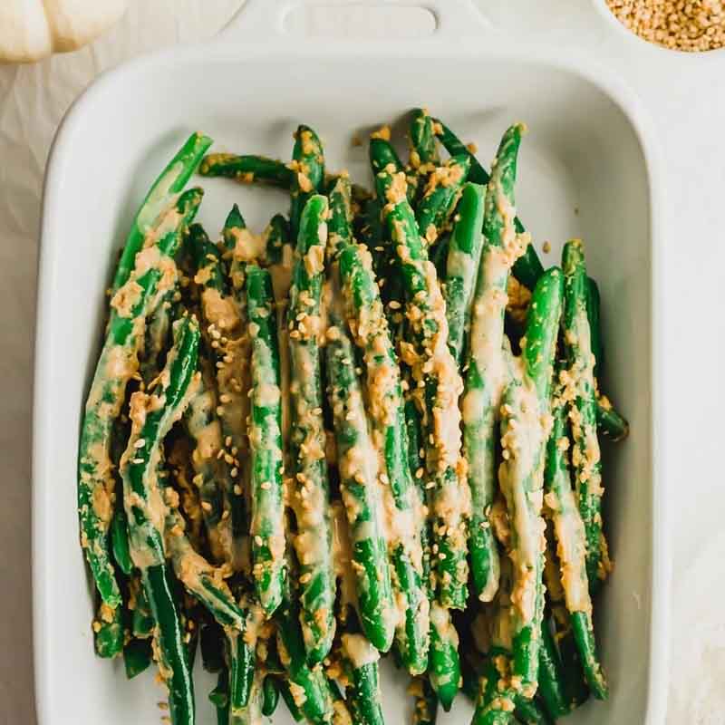 A casserole dish of fresh green beans with a miso tahini sauce. Recipe from Sift & Simmer.
