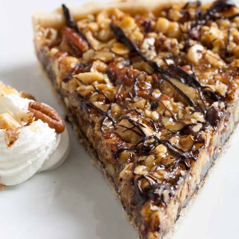 A slice of a nut & honey tart, drizzled with chocolate next to a dollop of whipped cream. Recipe by What A Girl Eats.