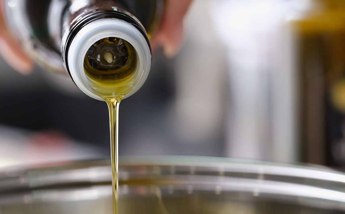 Olive oil pouring out of the bottle and into a pan for frying