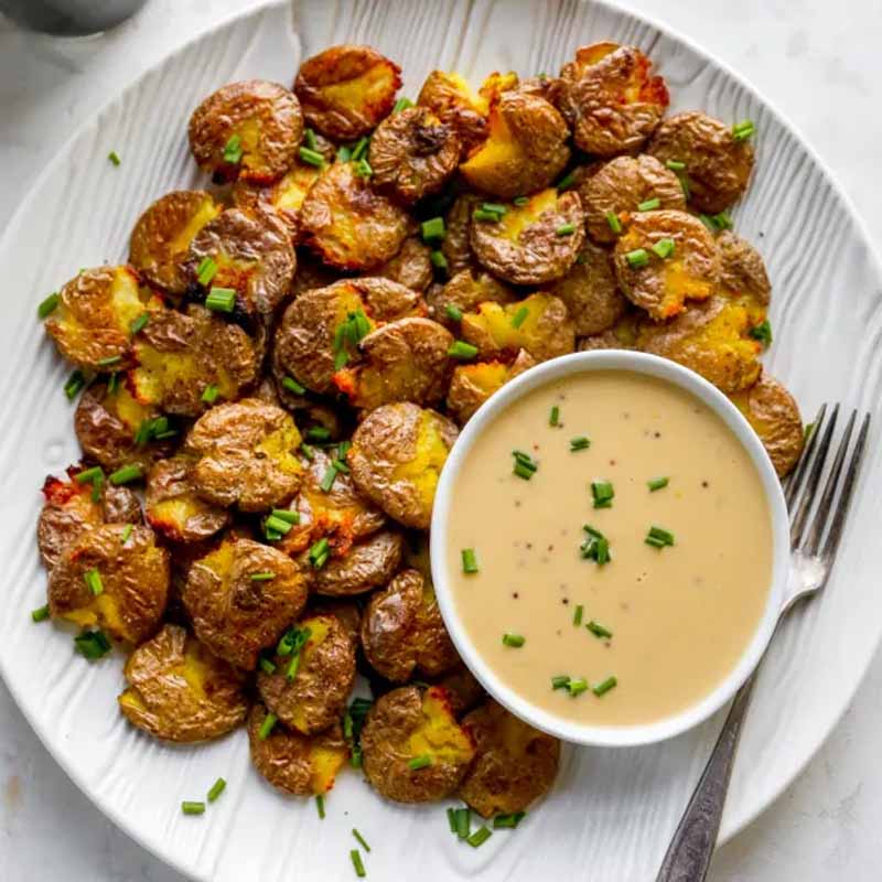Smashed potatoes on a white plate with a stout cheddar sauce. Recipe by Yes to Yolks.