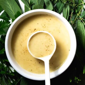 A spoon of turkey gravy made without drippings, on a bed of fresh herbs.