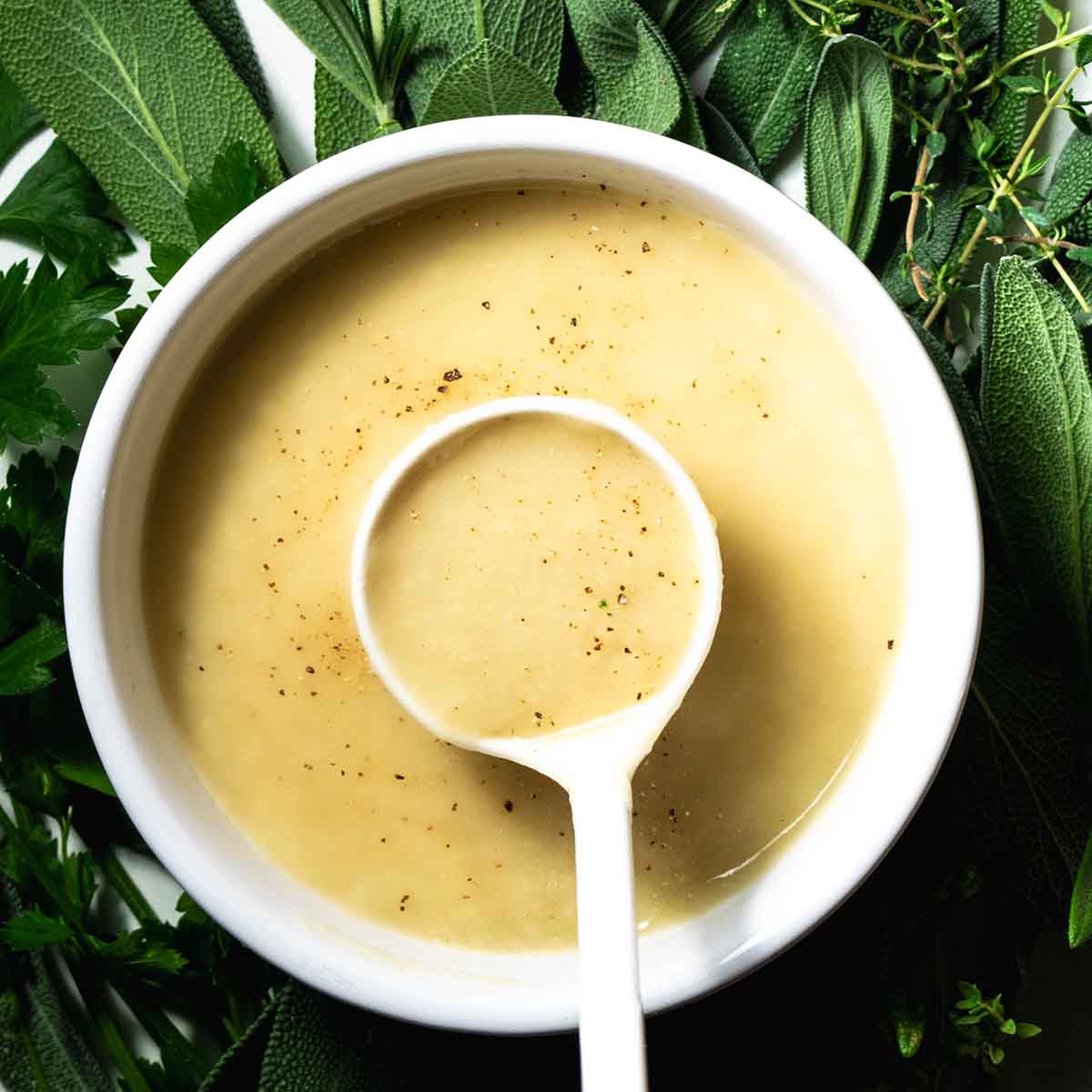 A spoon of turkey gravy made without drippings, on a bed of fresh herbs.