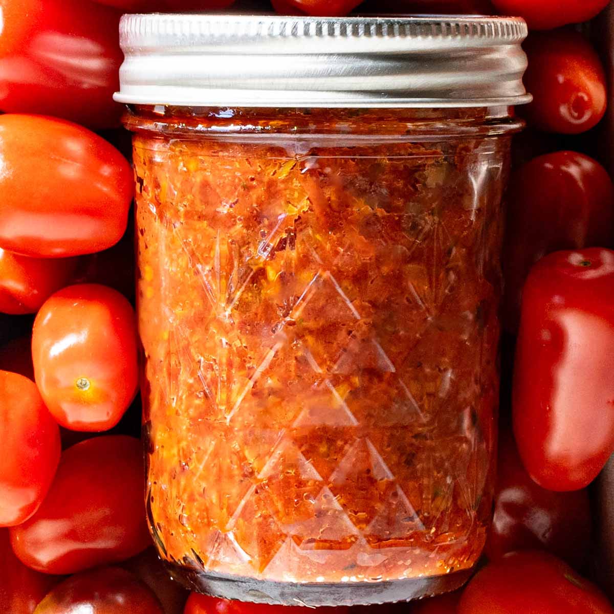 A jar of pizza sauce on garden tomatoes to show a recipe for canning.