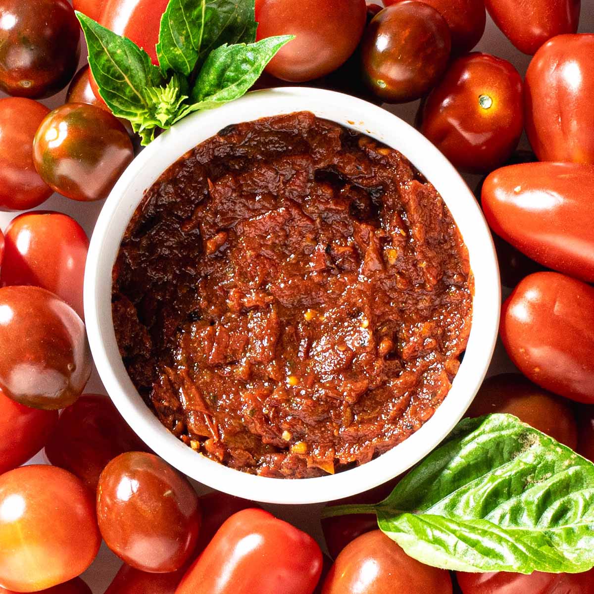 A bowl of homemade pizza sauce with fresh tomatoes and basil on a table.