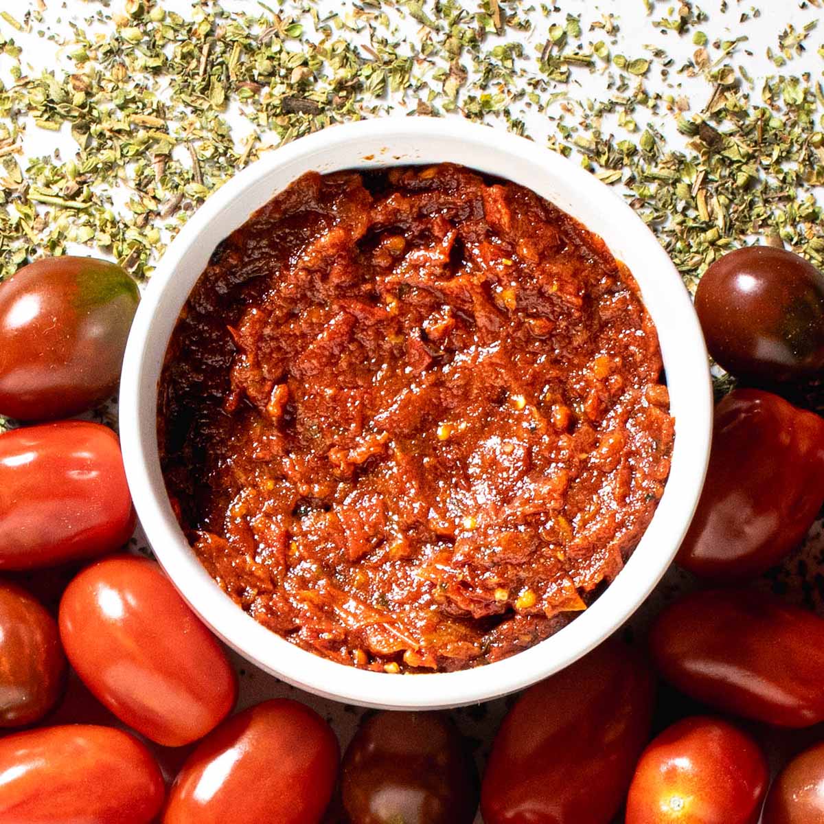 A bowl of pizza sauce from a recipe specifically made for canning. Surrounded by garden tomatoes and dried herbs.