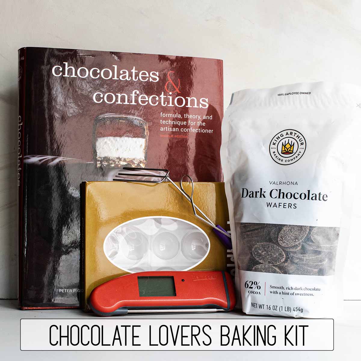 A gift kit for a baker who loves chocolate: a cookbook, bonbon moulds, thermometer, chocolate dipping tools, and valrhona chocolate wafers for tempering.