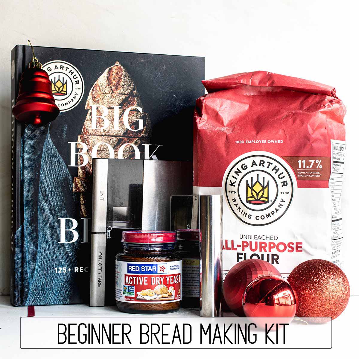 A beginner bread making kit that includes a cookbook, flour, yeast, a scale, and a bench scraper.