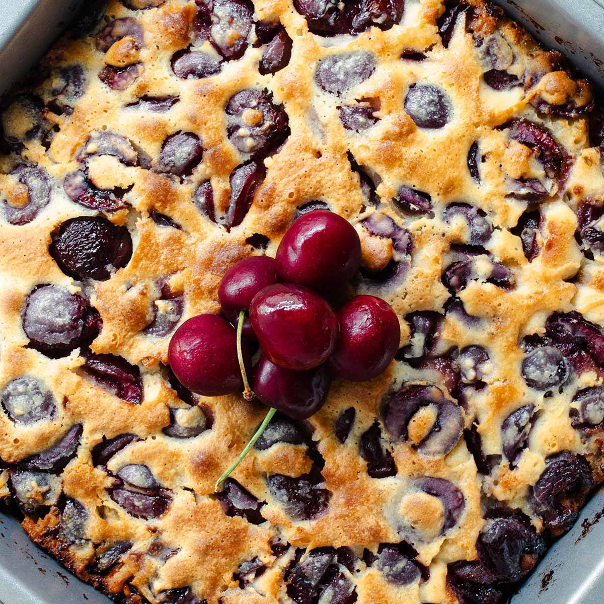 A cherry cobbler topped with fresh cherries, fresh from the oven