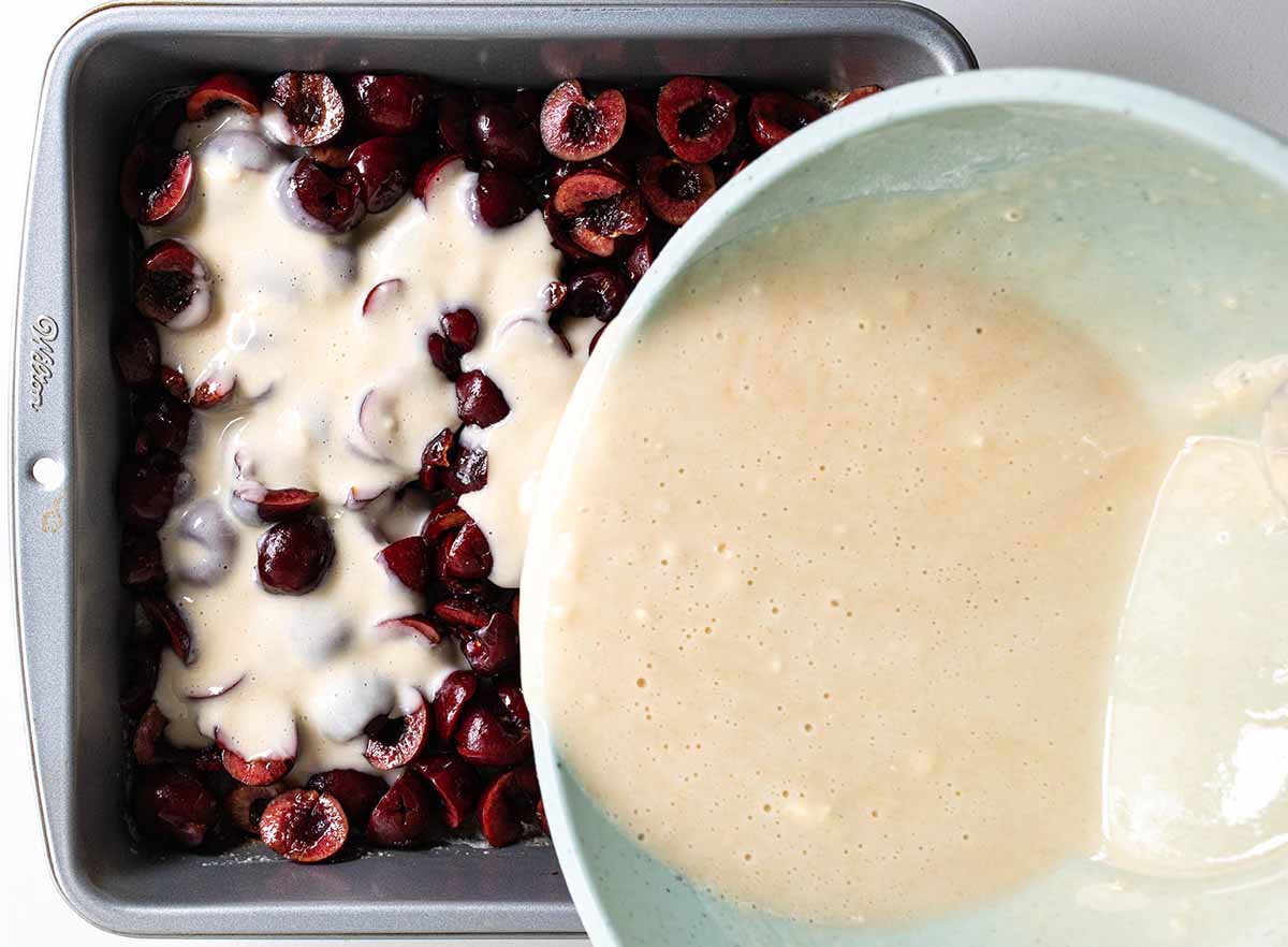 Batter pouring over fresh cherries to show how to make a cherry cobbler.