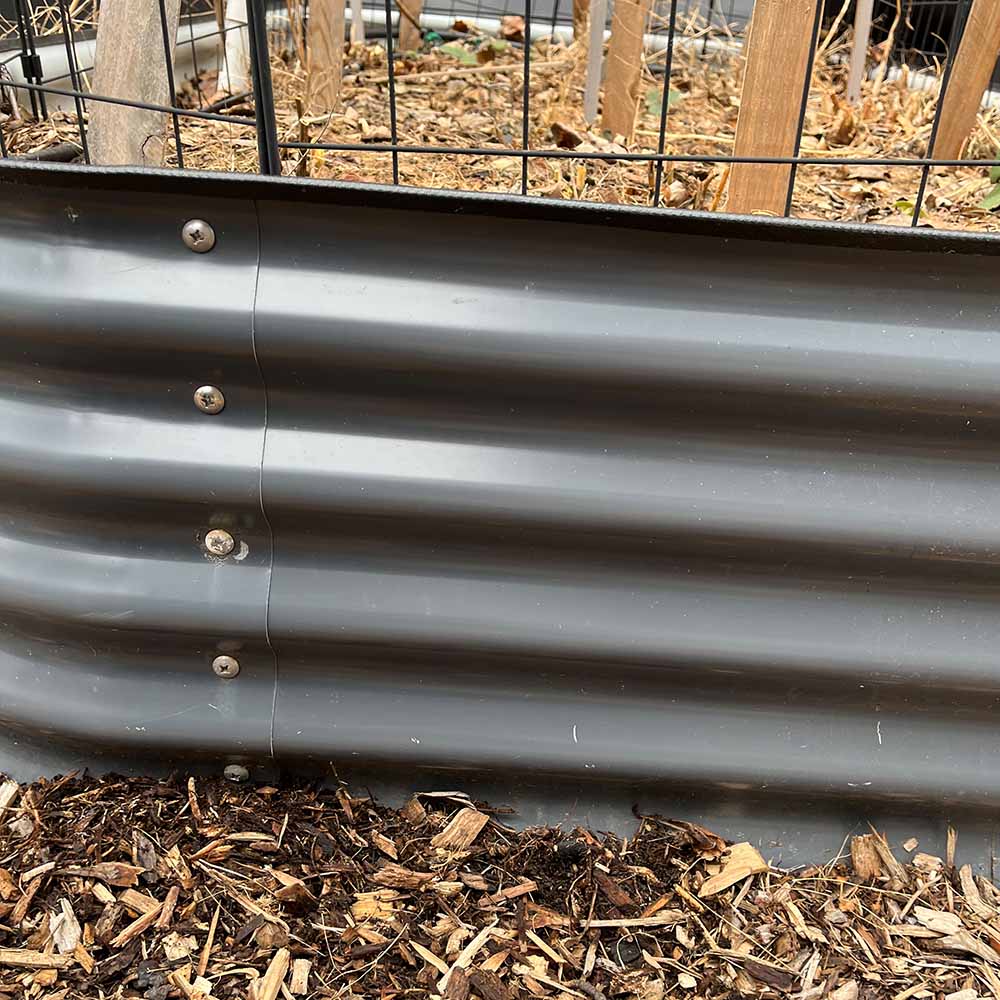A gray raised metal garden bed in the ground with no bottom