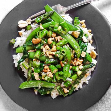 Stir fry with asparagus, snap peas, and spinach over rice, on a gray plate.
