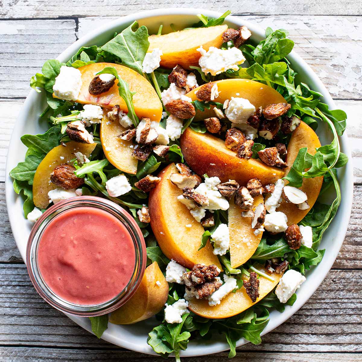 A peach arugula salad with feta cheese, pecans, and a raspberry vinaigrette.