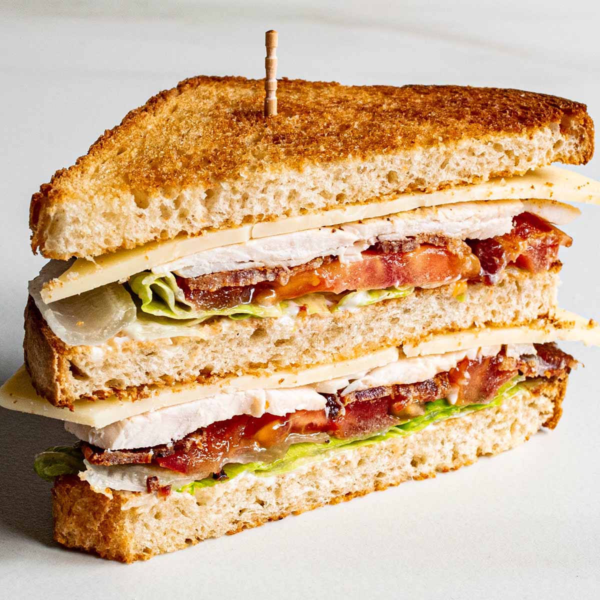 A club sandwich cut in half to show the distinct layers: toast, mayo, lettuce, tomato, bacon, and turkey. 