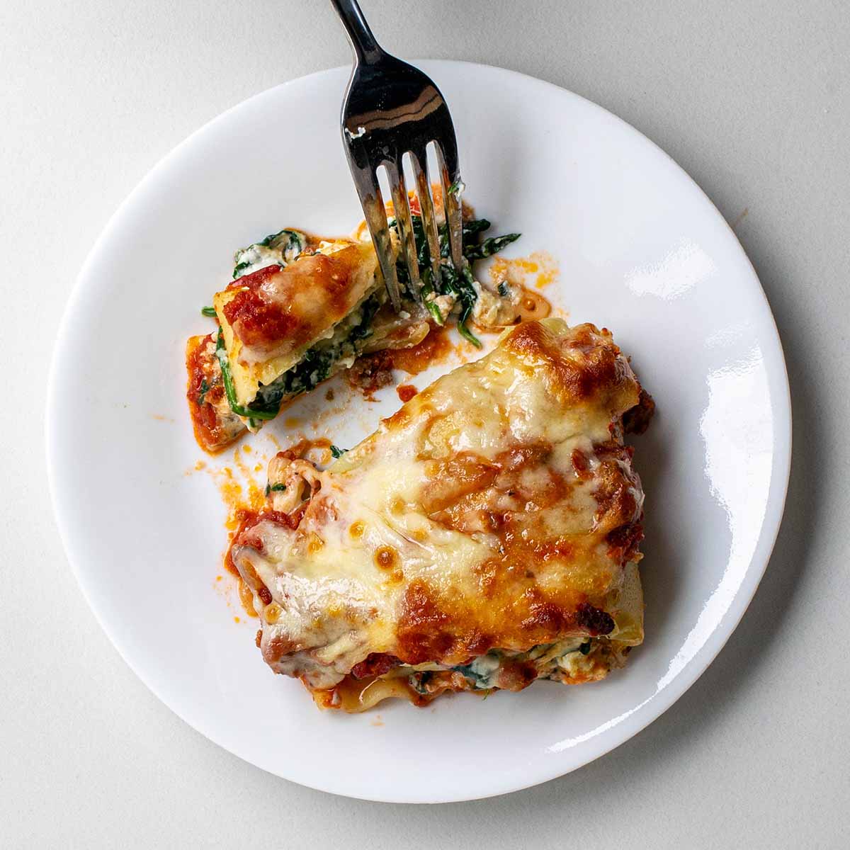A lasagna roll up cut with a fork to show the filling stays in place and doesn't fall apart.